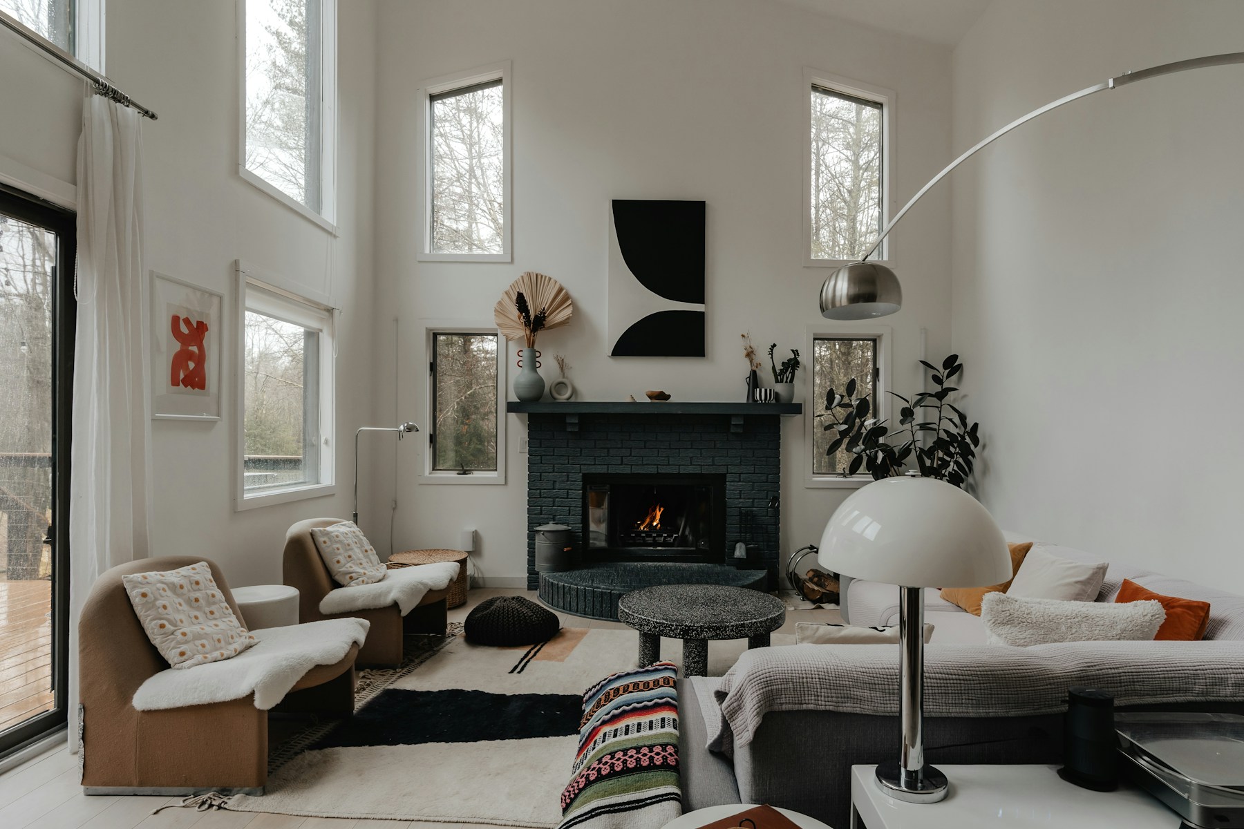 Grey and white living room with a charcoal fireplace and soft daylight through forest-facing windows